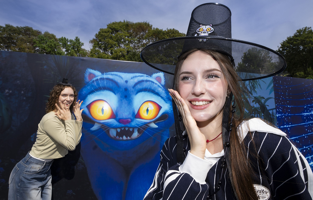 Two visitors posing in front of a large illustration of Derpy, the tiger character from KPop Demon Hunters.
