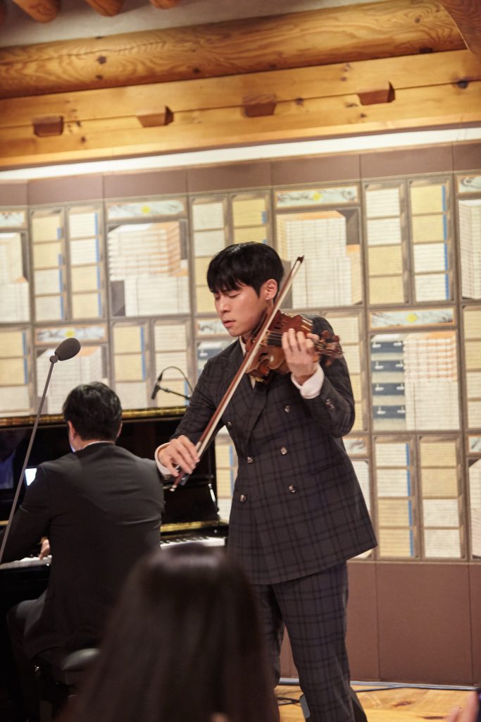 Musician Danny Koo plays the violin during a performance at Gala de LEBEIGE, accompanied by a pianist in a traditional Korean setting.