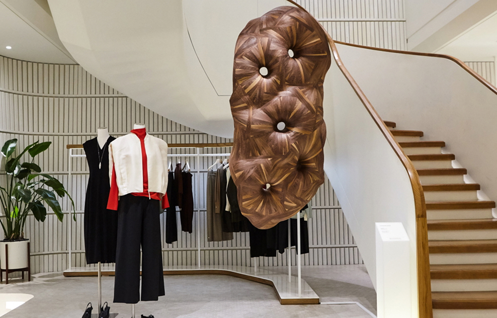 Exhibition space of Salon de LEBEIGE at ZIP739 Hannam featuring Heechan Kim’s wooden sculpture displayed near a staircase, with mannequins dressed in LEBEIGE’s capsule collection pieces.