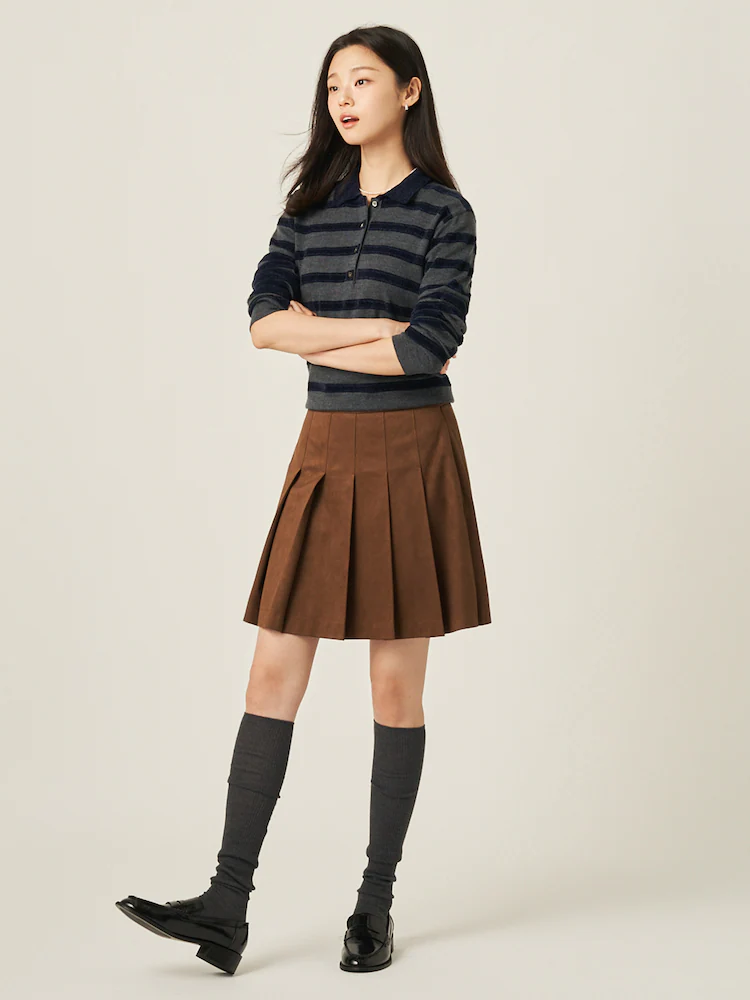 Model wearing a brown suede pleated mini skirt with a striped navy knit and knee-high socks for a classic fall look.