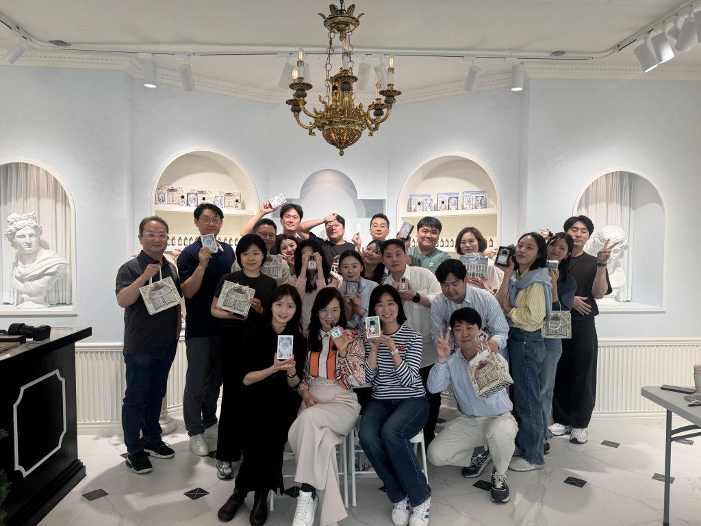 Samsung C&T’s DxP Business Strategy Team during a workshop posing together indoors, smiling and holding up decorative craft items in a bright room with white sculptures and classical-style decor.
