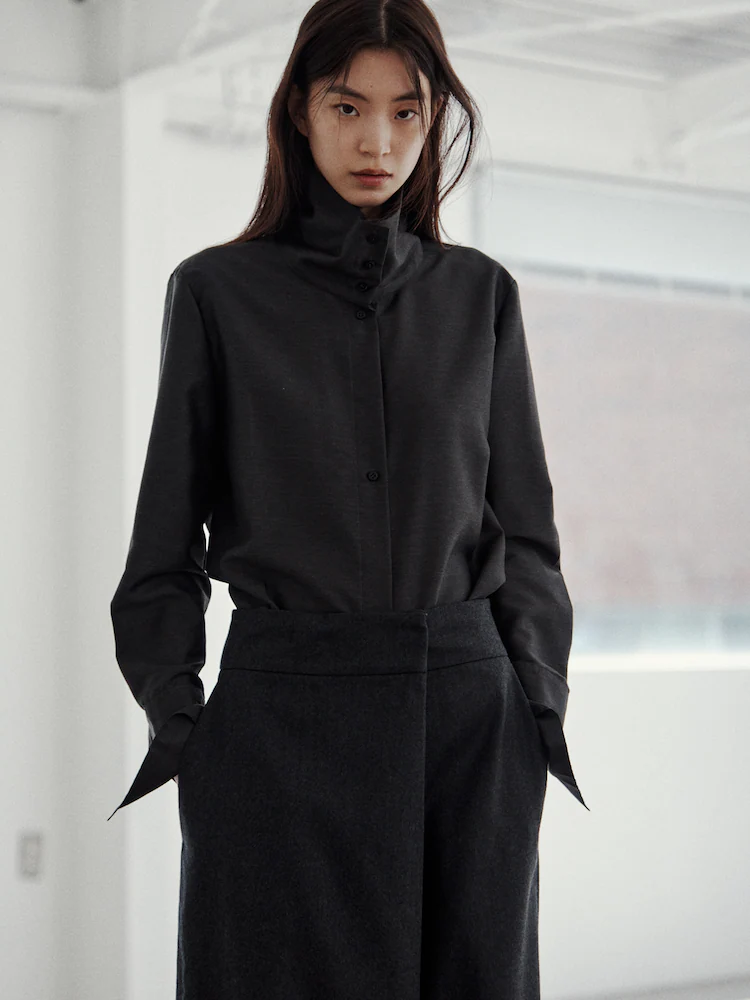 Model dressed in a dark brown silk blouse and black trousers, highlighting KUHO’s sophisticated modern tailoring.