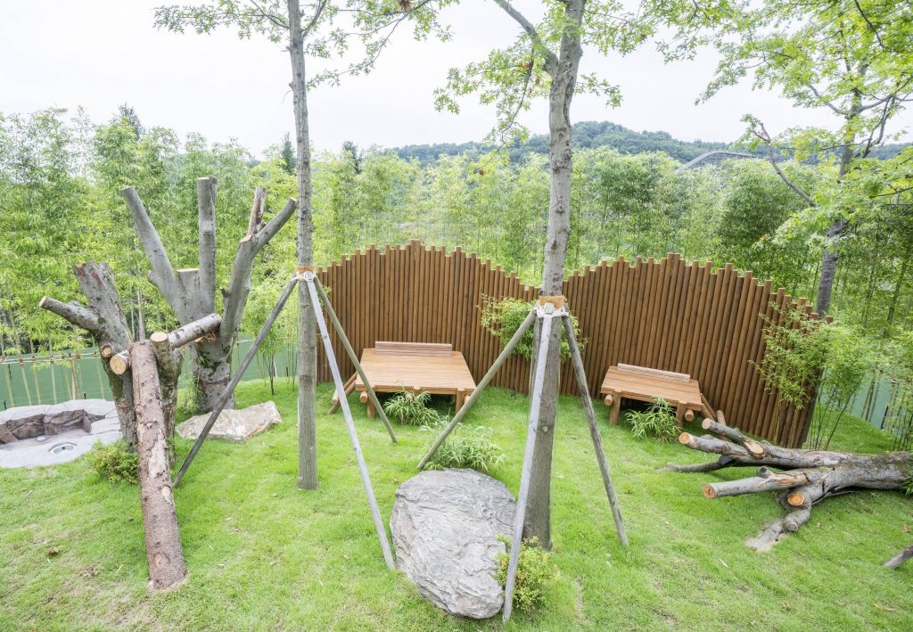 Wooden platforms, tree trunks, and shaded areas set up in Everland’s outdoor Panda Second House enclosure surrounded by greenery.