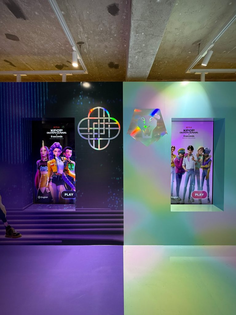 Interior photo of the 8seconds x K-Pop Demon Hunters pop-up store showing colorful wall projections and digital artwork of “Huntrix” and “Saja Boys” alongside the Netflix collaboration branding.