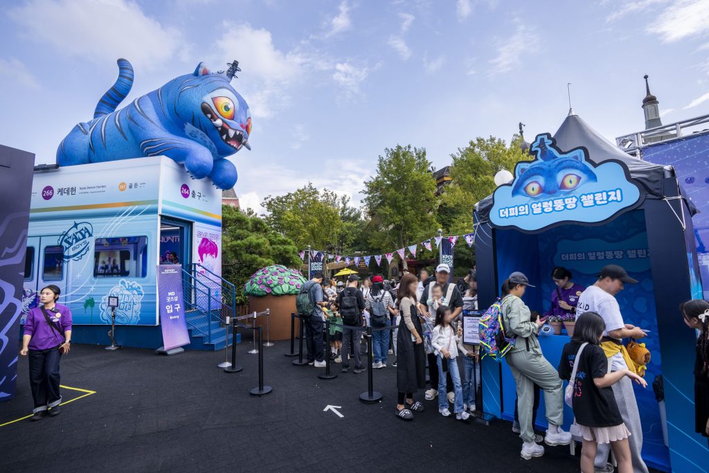 Visitors queuing outside Everland’s K-Pop Demon Hunters zone with a large blue character statue overhead.