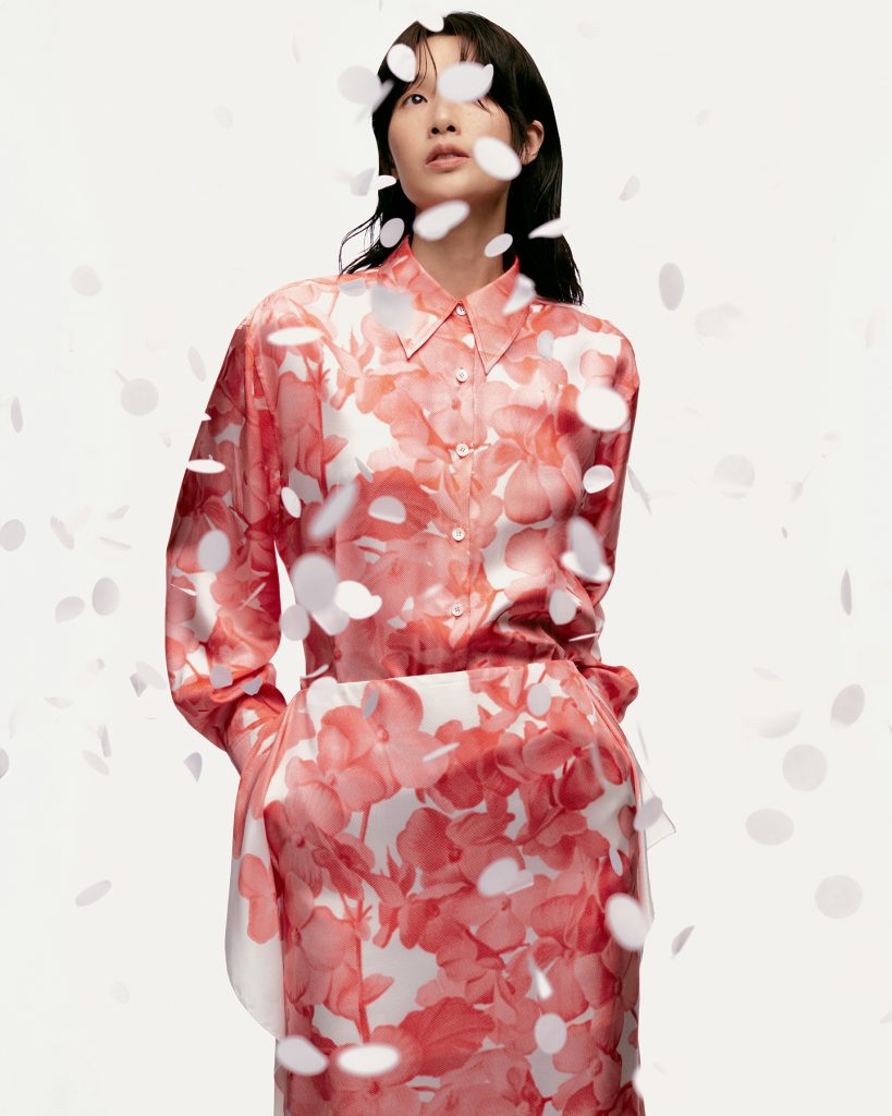 Model wearing a pink floral-print shirt and skirt from the JADEN CHO collection, photographed against a white background with falling white confetti.