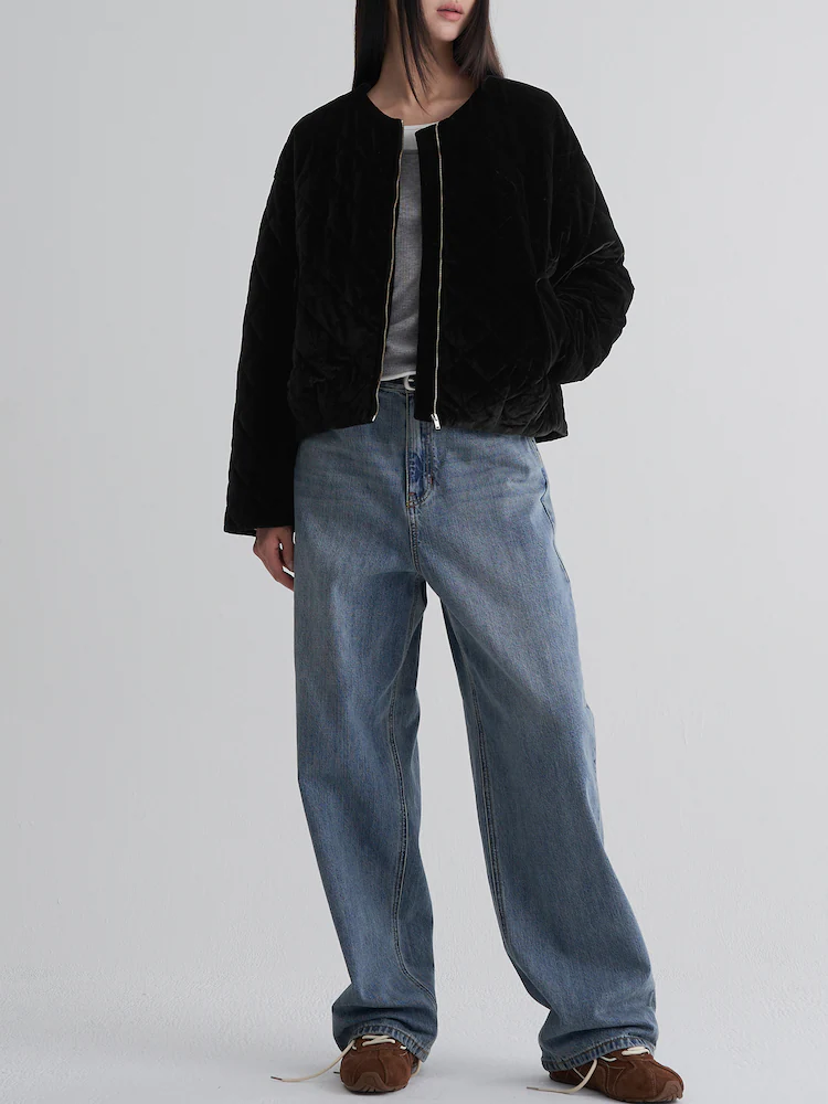 Model wearing a black diamond-quilted velvet padded jacket styled with a gray top and wide-leg denim against a light gray studio backdrop.