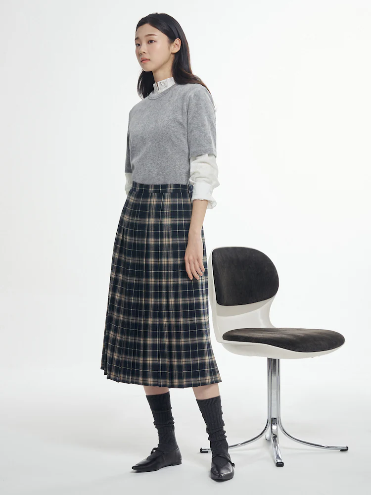 Model wearing a grey velvet half-neck T-shirt layered over a white blouse, paired with a navy plaid skirt while posing against a light studio backdrop.