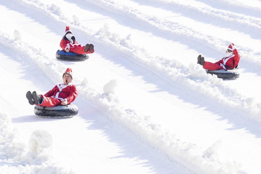 Visitors wearing Santa costumes ride snow tubes down the Snow Buster sledding lanes at Everland on a winter day.