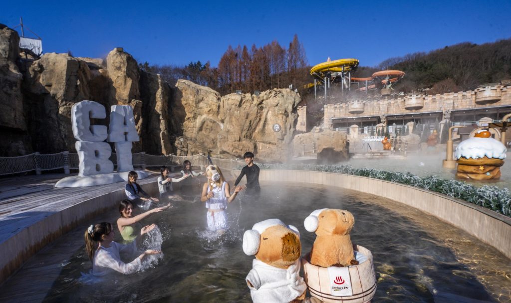 Visitors enjoy a heated outdoor spa pool at Caribbean Bay’s Winter Spa Cabi, with steam rising from the water and winter-themed decorations surrounding the area.