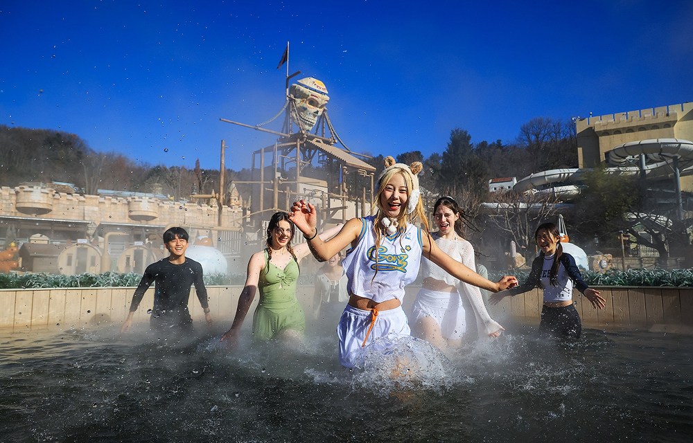 A group of guests splashes through a heated outdoor pool at Caribbean Bay’s Winter Spa Cabi, with bright blue skies and the waterpark’s themed structures in the background.