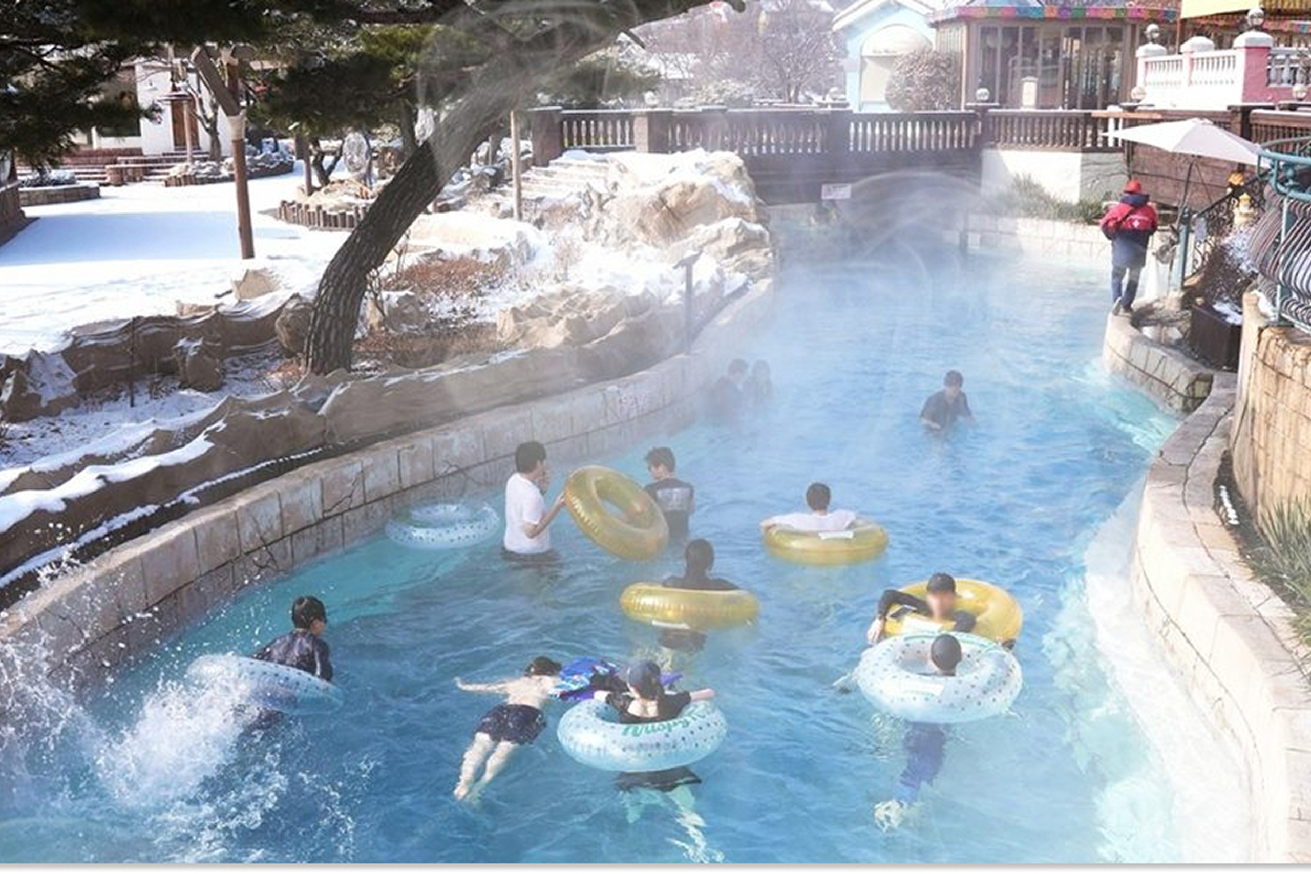 Visitors float on tubes along Caribbean Bay’s heated lazy river during winter, with steam rising from the water and snow visible around the attraction.