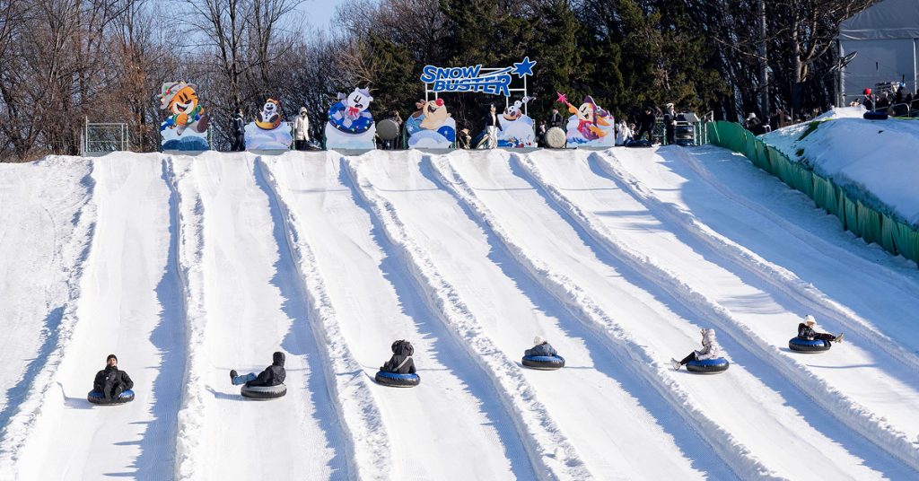 Visitors sliding down multiple lanes of the Snow Buster Express Course at Everland using large circular snow tubes during the winter season.