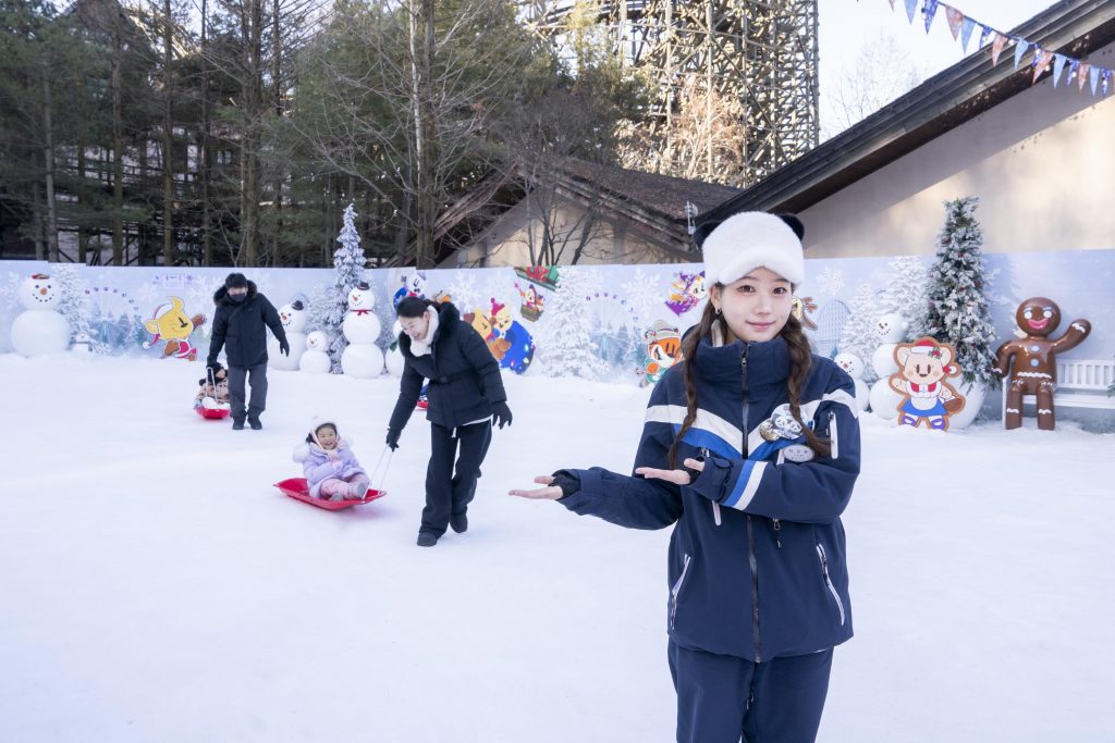 An Everland staff member stands in a snow play area while families and children enjoy sledding and snow activities at the Snow Play Ground during the winter season.