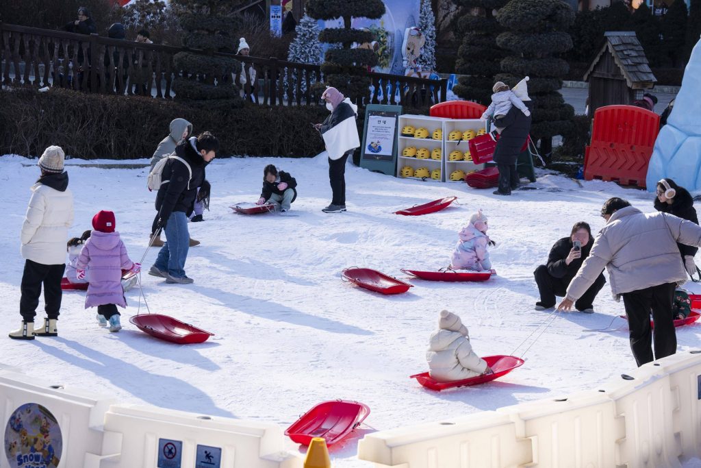 Children and families play in the snow using small sleds at Everland’s Snow Yard, a family-friendly snow play area during winter.