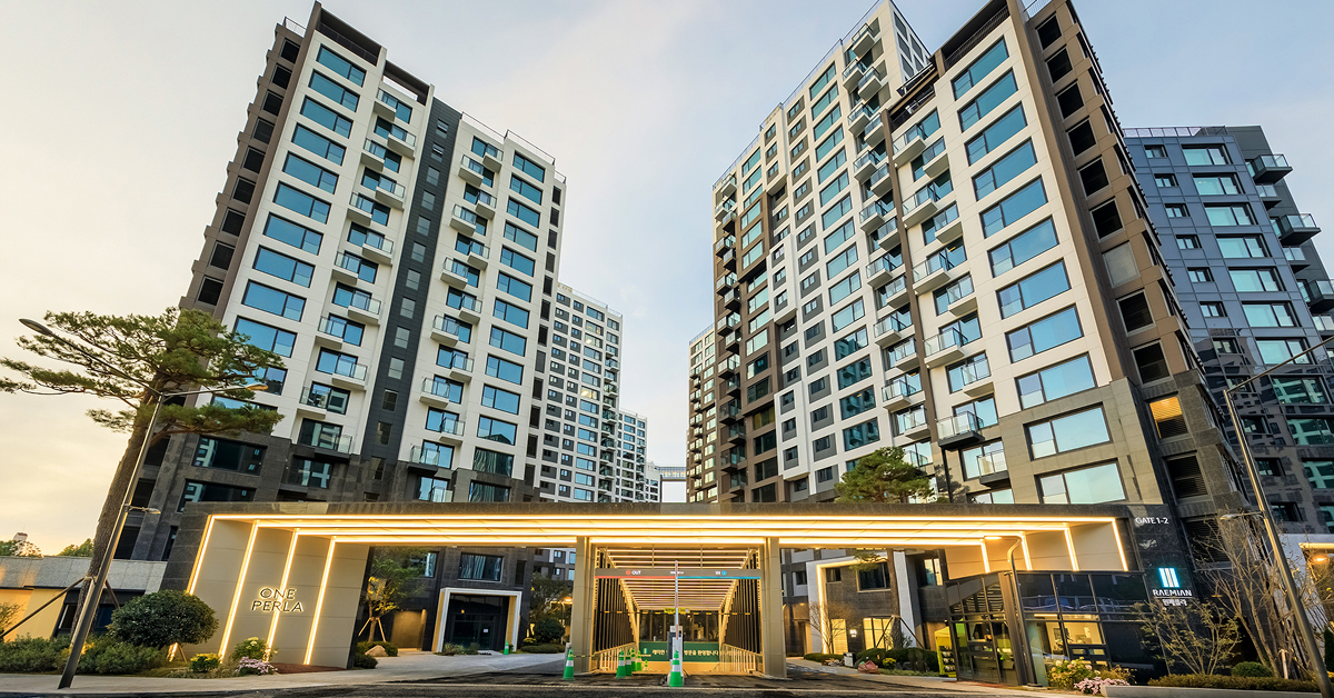 Exterior view of Raemian One Perla apartment towers and illuminated entrance gate showcasing modern façade design and landscaping.
