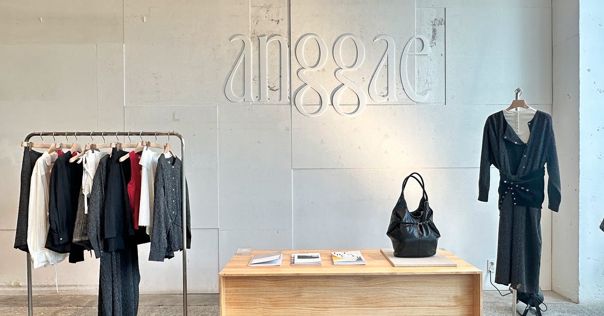 Interior view of anggae’s 2026 Spring pop-up store at Beaker Cheongdam, featuring neutral-toned womenswear displayed on a clothing rack, a wooden table with accessories, and the brand logo on a minimalist wall.