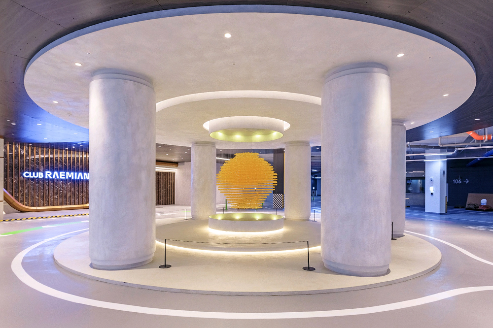 Interior view of Club Raemian at Raemian One Pentas featuring large circular ceiling elements, structural columns, and a central illuminated art installation.