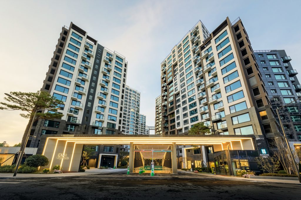 Exterior view of Raemian One Perla apartment towers and illuminated entrance gate showcasing modern façade design and landscaping.