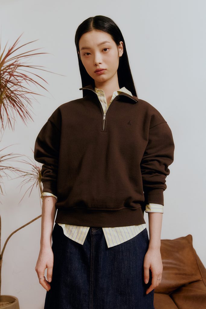 Female model wearing a brown quarter-zip sweatshirt layered over a striped shirt with a denim skirt from BEANPOLE LADIES SS 2026 collection.