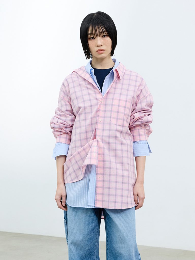 Model wearing a pink check shirt layered over a blue striped shirt with denim pants from SAND SOUND’s SS 2026 collection.