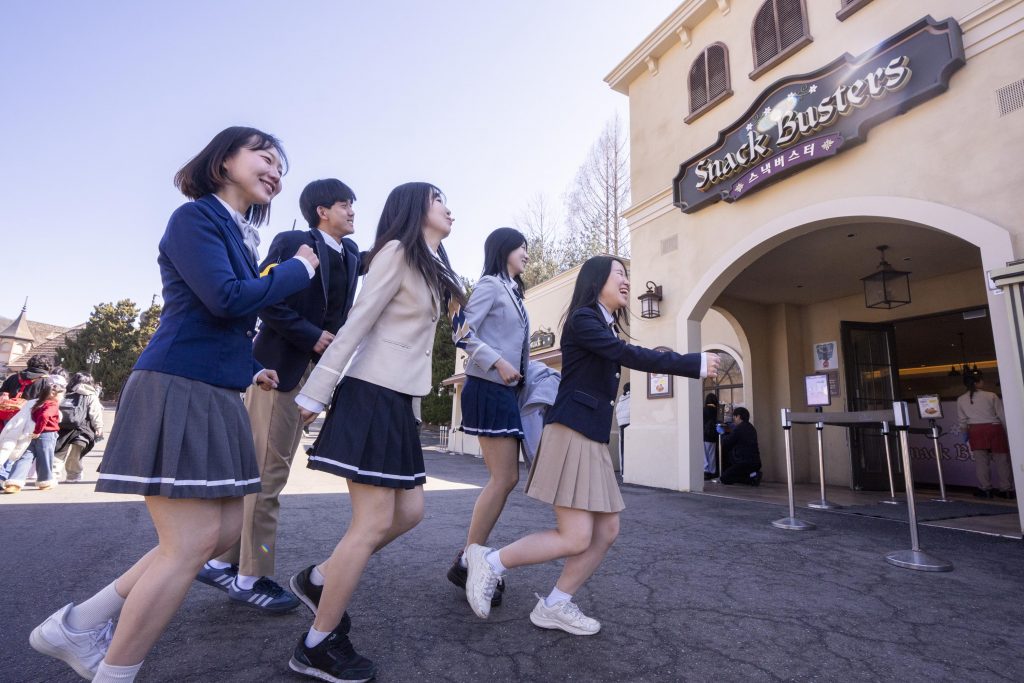 A group of visitors dressed in school uniforms walk toward the Snack Buster restaurant at Everland as part of the School of Spice themed program.