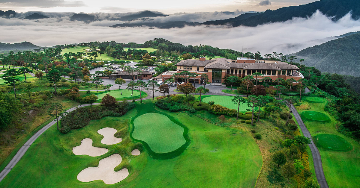 Aerial view of Gapyeong Benest Golf Club with clubhouse, fairways, and surrounding mountains covered in morning mist.