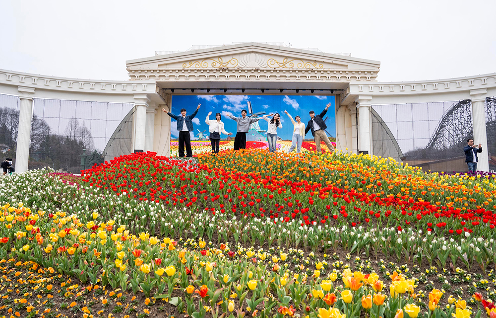 Group of visitors standing on a hillside covered with red, yellow, and white tulips in front of the Four Seasons Garden stage at Everland.