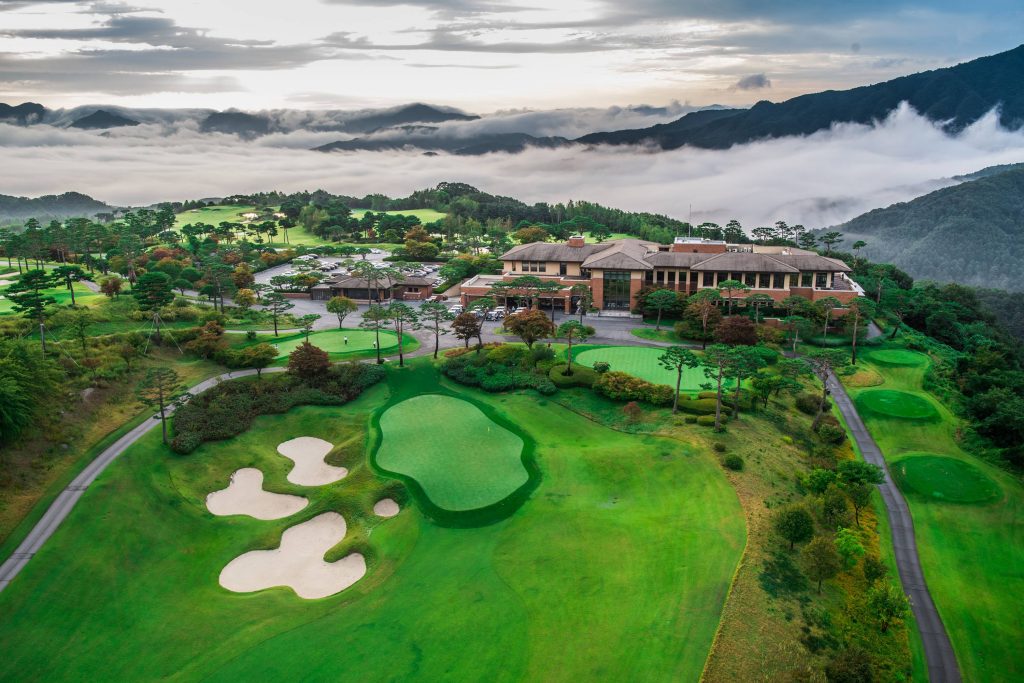 Aerial view of Gapyeong Benest Golf Club with clubhouse, fairways, and surrounding mountains covered in morning mist.