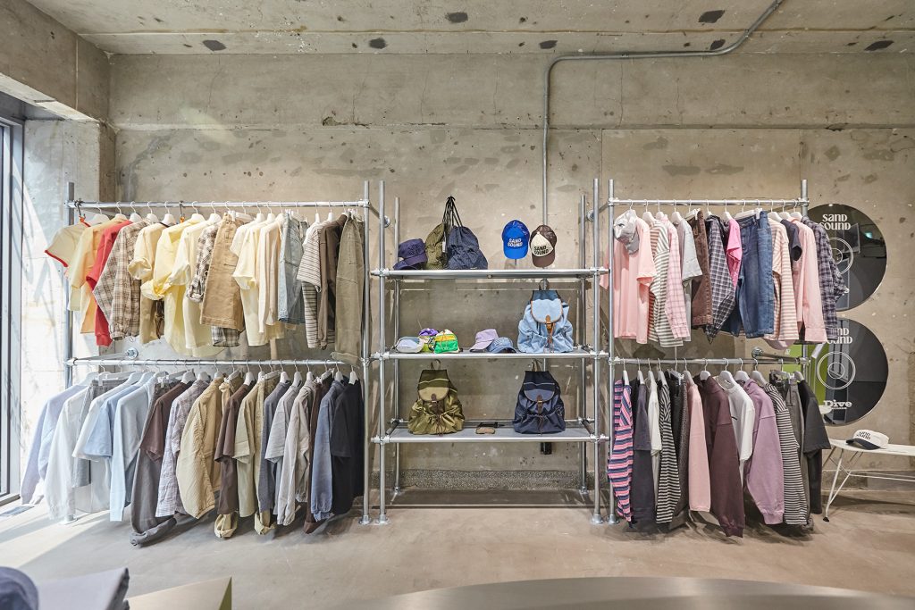 Clothing racks displaying SAND SOUND 26SS collection with layered casualwear, shirts, and accessories