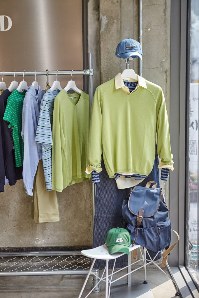 Green knit layered over shirt with backpack and cap from SAND SOUND 26SS collection