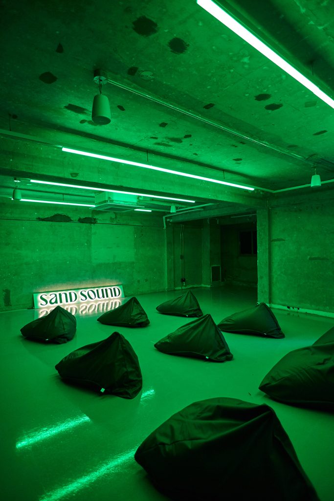 Green-lit immersive room at SAND SOUND 26SS pop-up with seating and branded sign