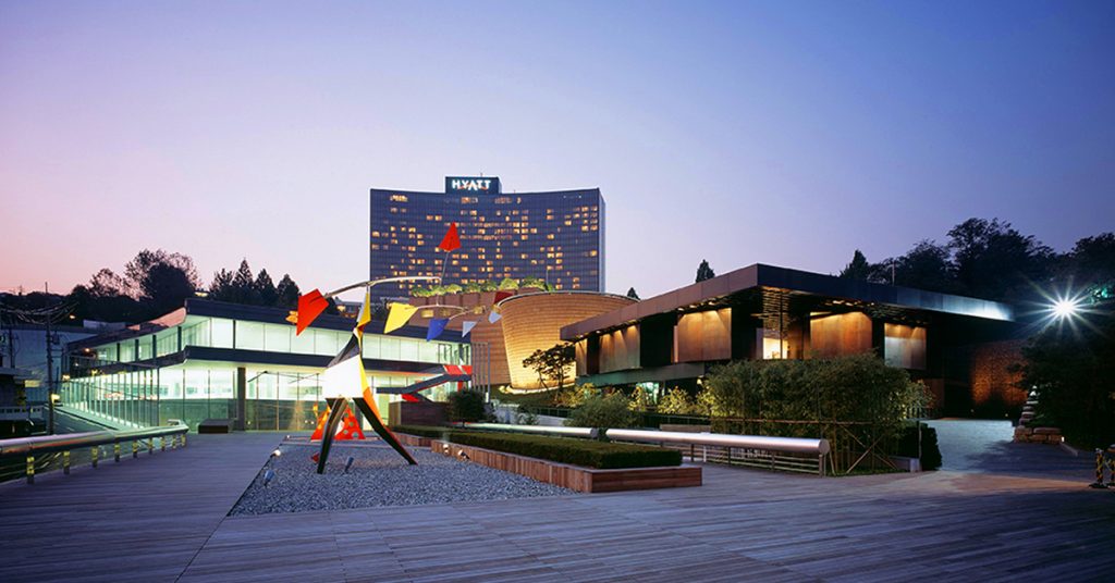 Exterior view of Leeum Museum of Art in Seoul, showing the museum’s glass, brick, and dark-toned buildings with a tall reflective sculpture displayed in the outdoor courtyard.