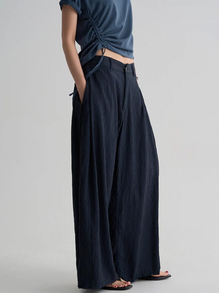 Model wearing 8seconds ALL-DAY CREASE Side-Tuck Pants in navy with a blue top and white layer tied at the waist.