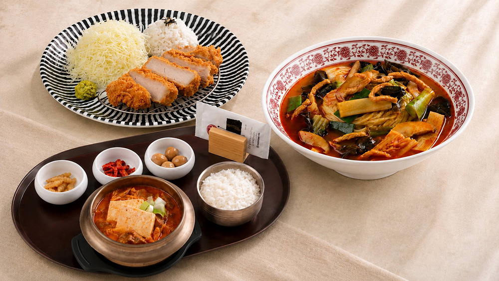 Three Everland signature dishes arranged on a table: kimchi stew with rice and side dishes, spicy seafood noodle soup, and handmade roast pork cutlet with shredded cabbage.