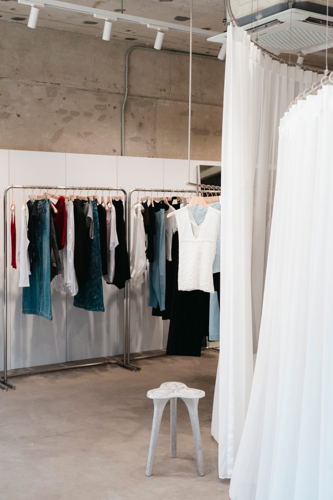 Interior of the ‘anggae’ 26SS pop-up store with clothing racks, sheer white fabric curtains, and womenswear displays.