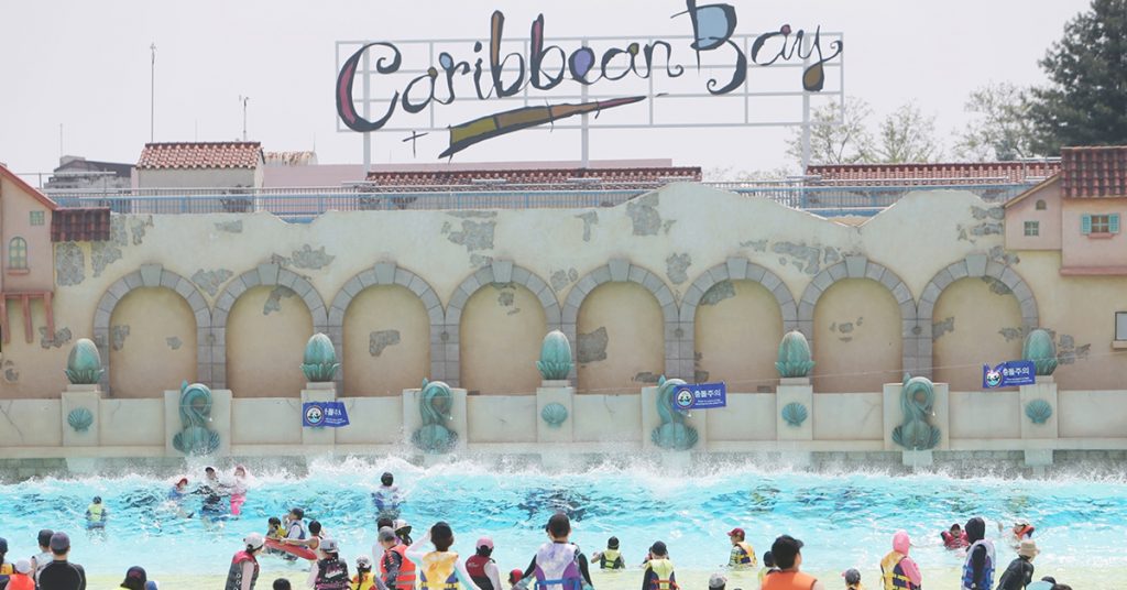 Visitors wearing life jackets enjoy waves at Caribbean Bay’s outdoor Wave Pool under the Caribbean Bay sign.