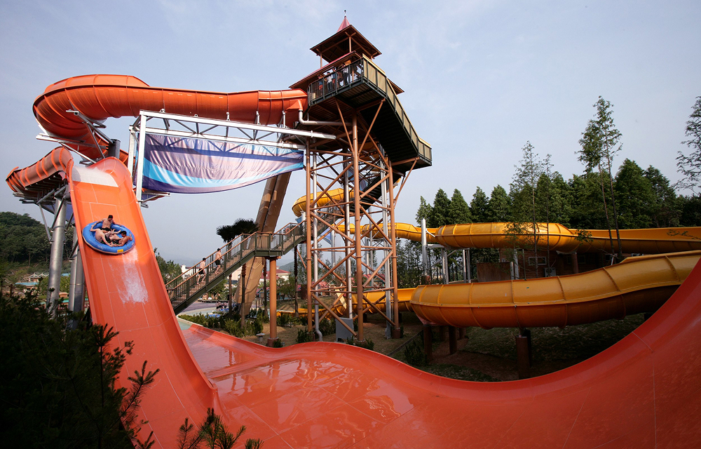 Riders descend on an orange raft slide at Caribbean Bay’s Tower Boomerang Go, surrounded by colorful water slide structures.