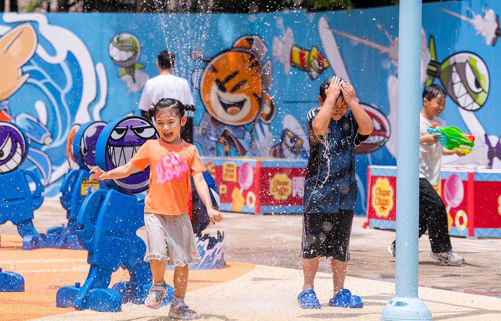 Children smile and play under water sprays at Everland’s Water Pangpang Adventure, with colorful character figures and water game booths in the background.