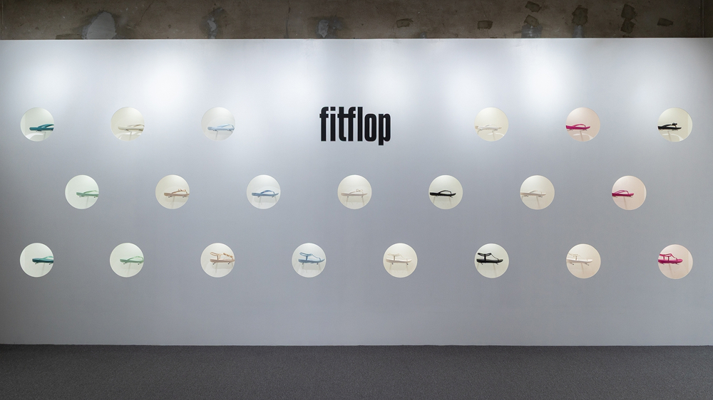 Wall display inside FitFlop’s Seongsu pop-up store showing multiple sandal styles arranged in circular lighted shelves under the FitFlop logo.