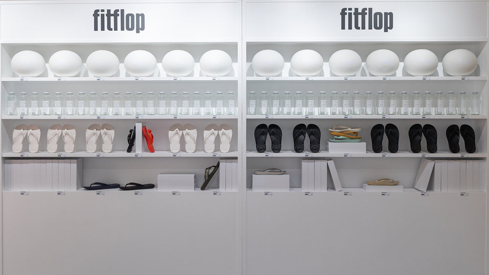 White FitFlop product shelves displaying sandals, flip-flops, round objects, and clear bottles inside the Seongsu pop-up store.