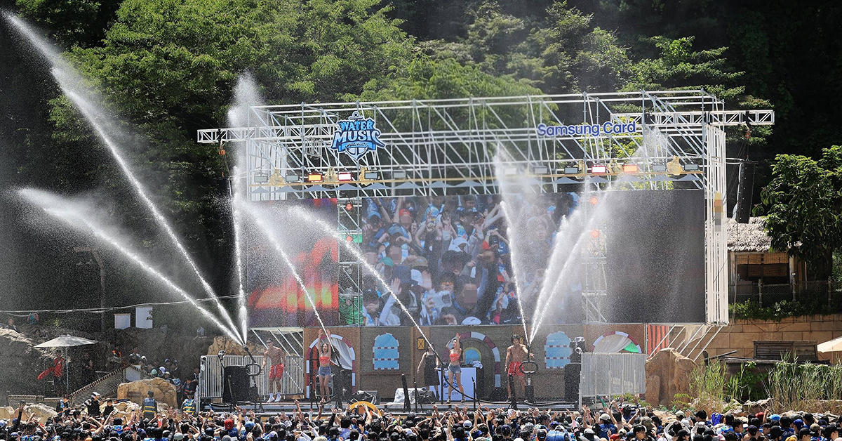 Visitors enjoy the Water Music Pool Party at Caribbean Bay’s outdoor wave pool, featuring live performances, water cannons, and a large LED stage