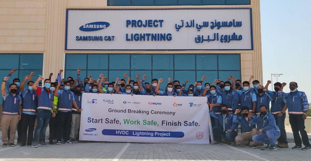 A large group of Samsung C&T employees and project partners pose outside the Project Lightning site office, raising their fists behind a banner reading, “Ground Breaking Ceremony — Start Safe. Work Safe. Finish Safe.”