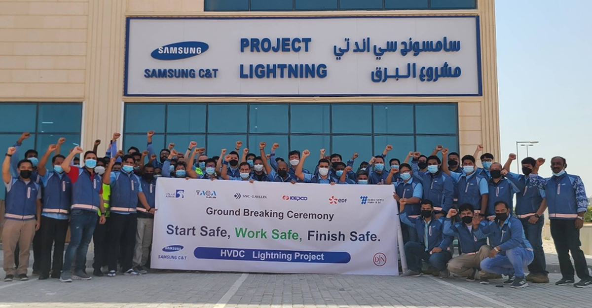 A large group of Samsung C&T employees and project partners pose outside the Project Lightning site office, raising their fists behind a banner reading, “Ground Breaking Ceremony — Start Safe. Work Safe. Finish Safe.”
