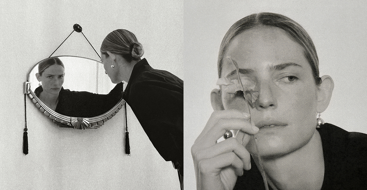 Model wearing a dark look from The Aperture’s Fall 2026 collection leaning toward a vintage wall mirror in a black-and-white photograph.