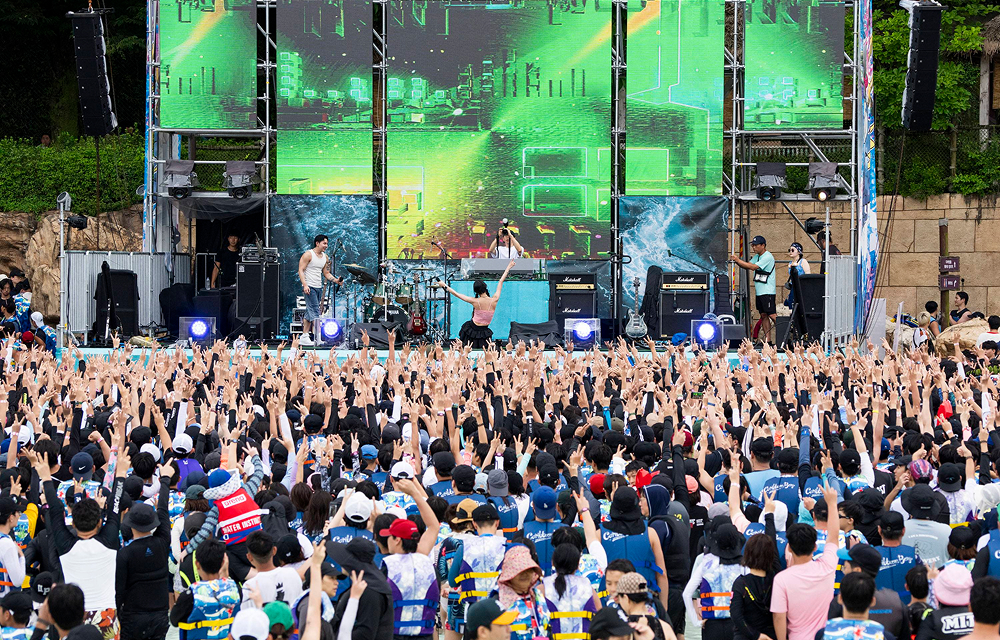 Visitors raise their hands and enjoy a live performance during the Water Music Pool Party at Caribbean Bay’s outdoor wave pool