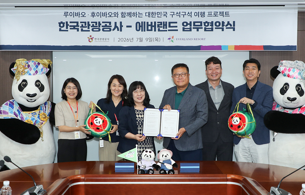 Representatives from Everland and the Korea Tourism Organization pose behind a conference table with the signed agreement, campaign items, and two panda mascots.