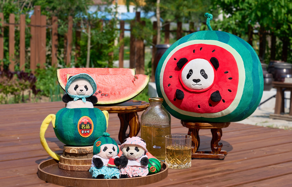 Gochang-themed panda merchandise is displayed with watermelon slices and drinks, including Rui-Hui travel companion dolls and large watermelon-shaped panda cushions.