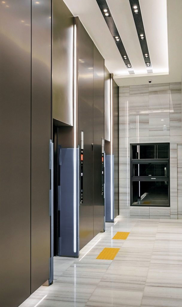 The common lobby at Raemian One Perla maximizes openness through high ceilings, vertical lighting, and refined stone finishes