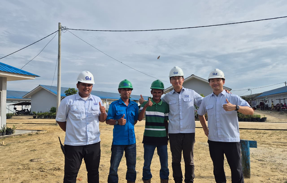 SNG employees and local workers wearing helmets pose together outdoors at a plantation site.